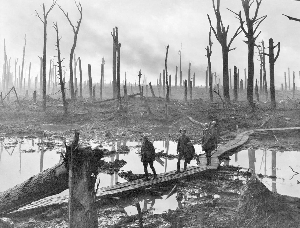 Battle of Ypres, 1917. Soldiers walk along a boardwalk over a muddy swamp surrounded by burnt trees.