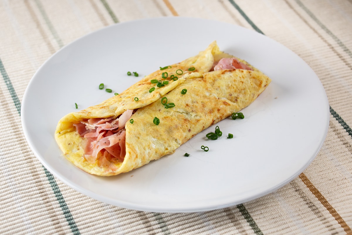 White plate with an omelette full of ham and cheese.