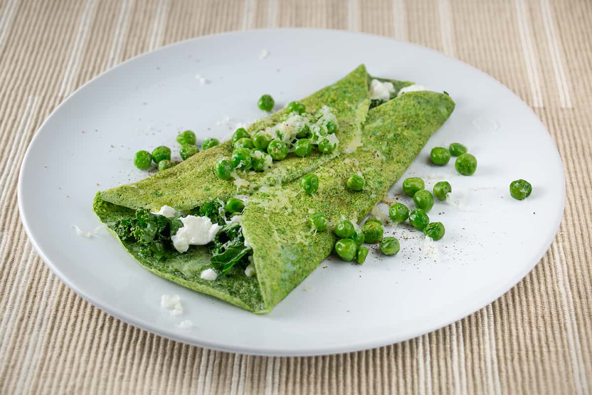White plate with a green omelette and peas.