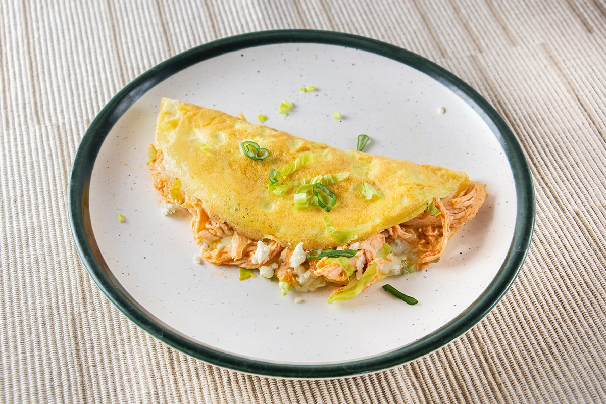 Omelette filled with chicken and celery in an orange sauce, all on a white plate with a green edge.