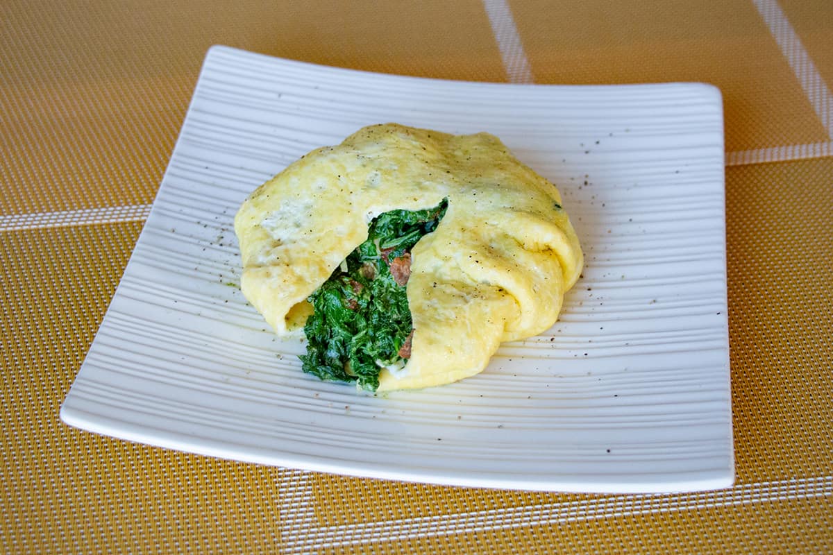 White square plate with a round omelette stuffed with creamy spinach.