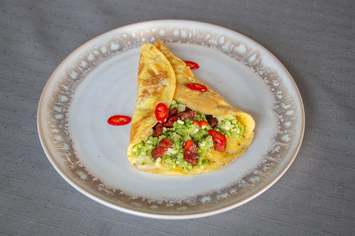 Omelette stuffed with green pea and pancetta mixture on a white plate.
