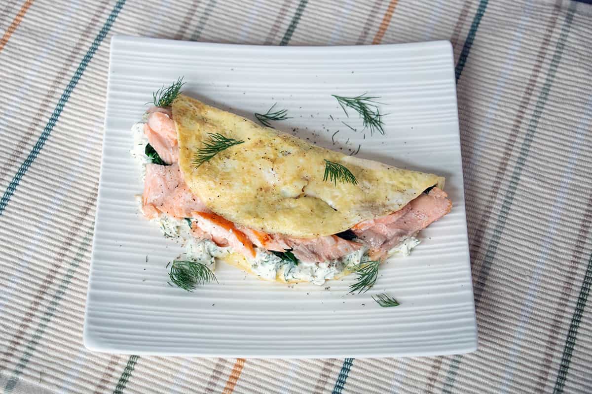 Square white plate with an omelette filled with salmon and cream cheese.