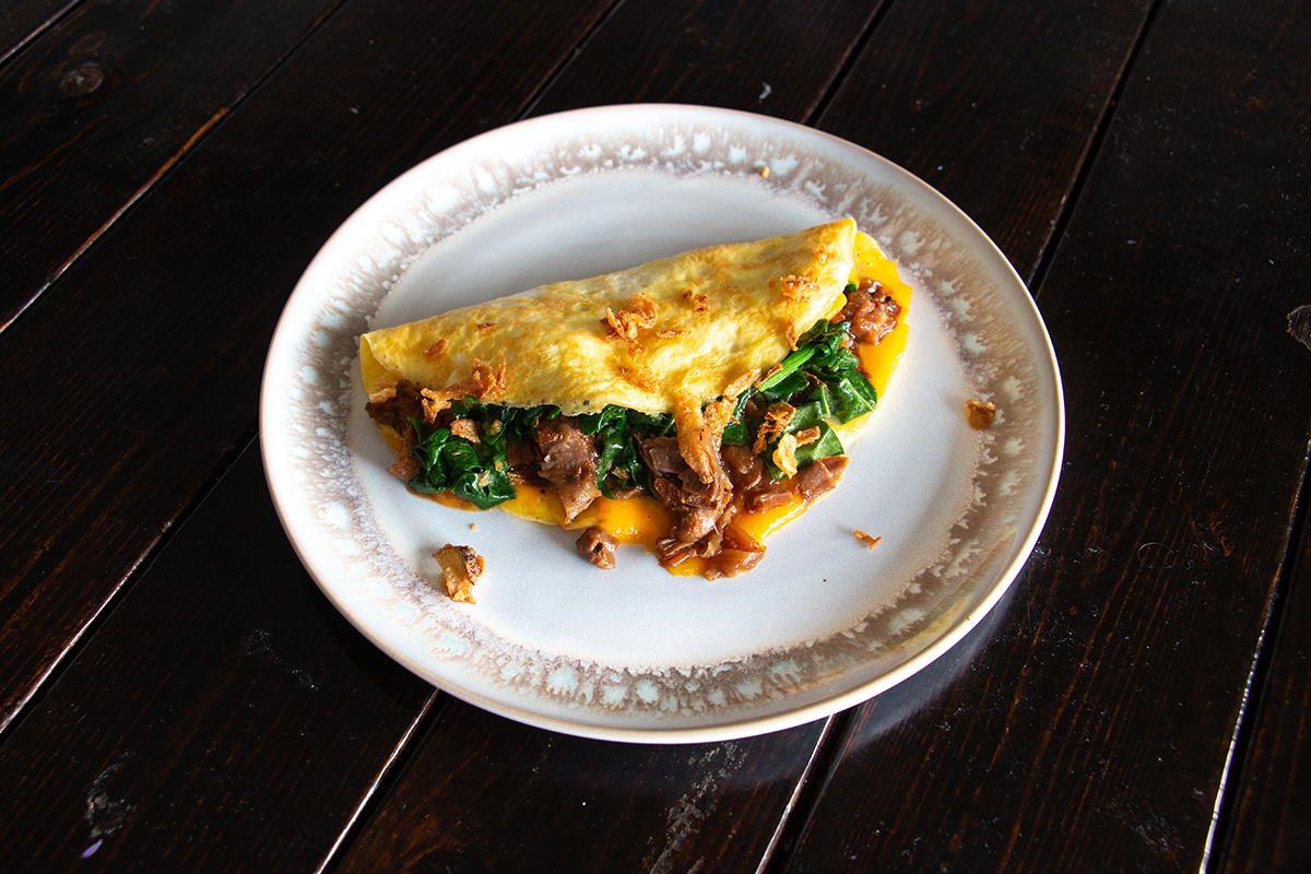 White and brown plate on a wooden table. An omelette with beef, spinach and cheese is on the plate.