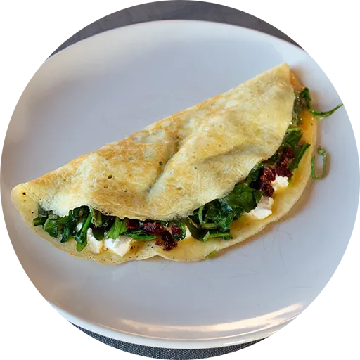 White plate with an omelette stuffed with spinach, goat cheese and sun-dried tomatoes.