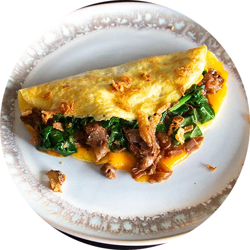 White and brown plate on a wooden table. An omelette with beef, spinach and cheese is on the plate.