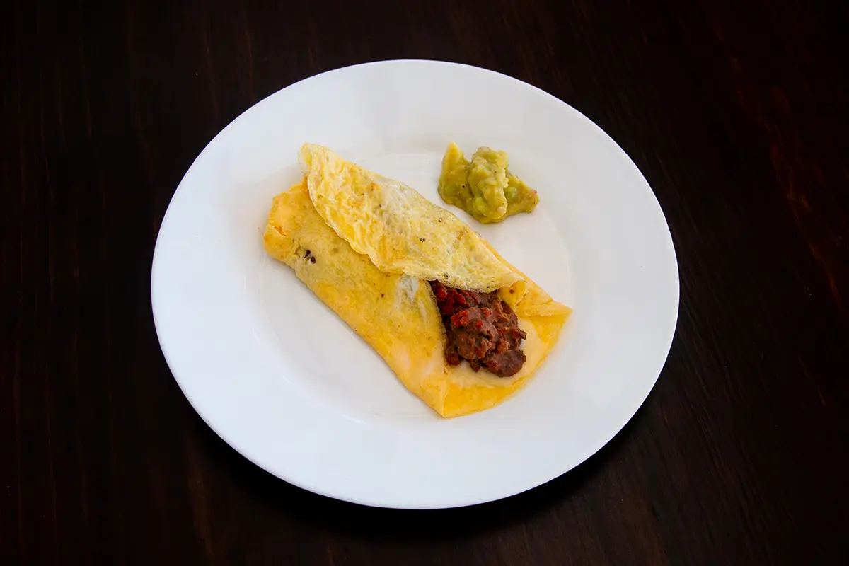 White plate with a burrito with an egg wrap.