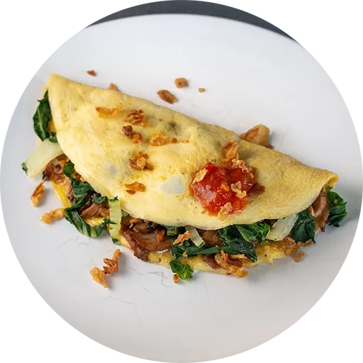 Omelette on a round white plate. It is filled with green bok choy and red bbq pork pieces.