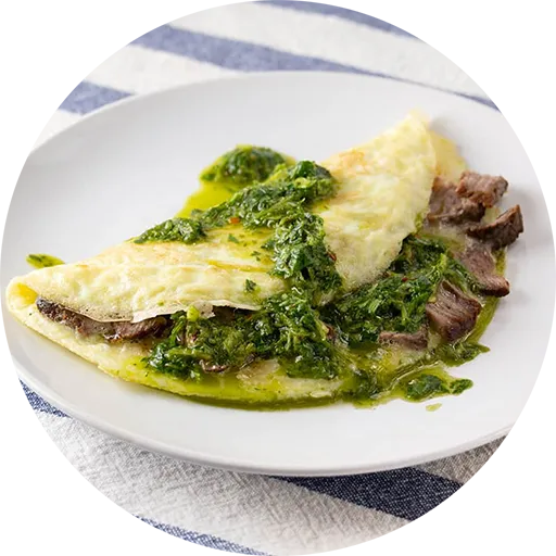 White plate with an omelette filled with steak and topped with a green sauce.