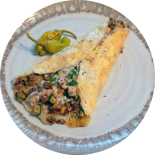 White and grey plate with a rolled omelette stuffed with roasted eggplant, zucchini, and a tahini yogurt sauce.