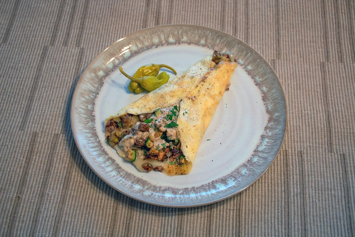 White and grey plate with a rolled omelette stuffed with roasted eggplant, zucchini, and a tahini yogurt sauce.