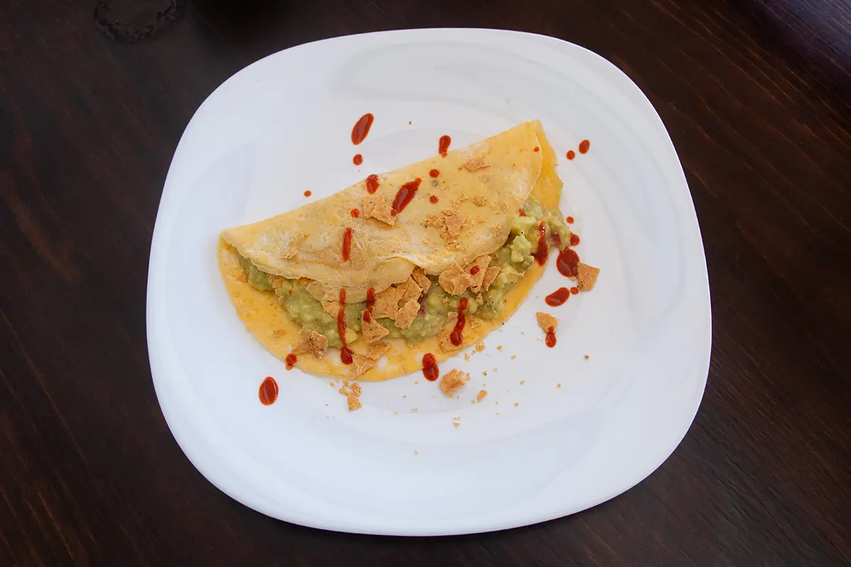 White plate with an omelette filled with guacamole and tortilla chips.