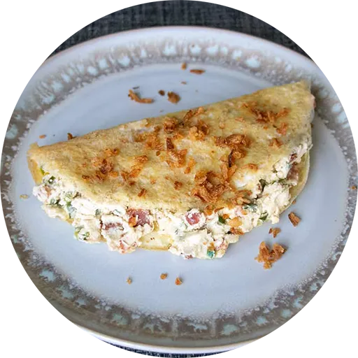 Omelette filled with cream cheese, jalapeños and bacon bits. Topped with fried onions and placed on a white plate.