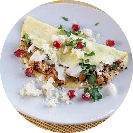 Omelette on a plate, filled with chicken & chickpeas, and topped with herbs, cheese and red pomegranate seeds.