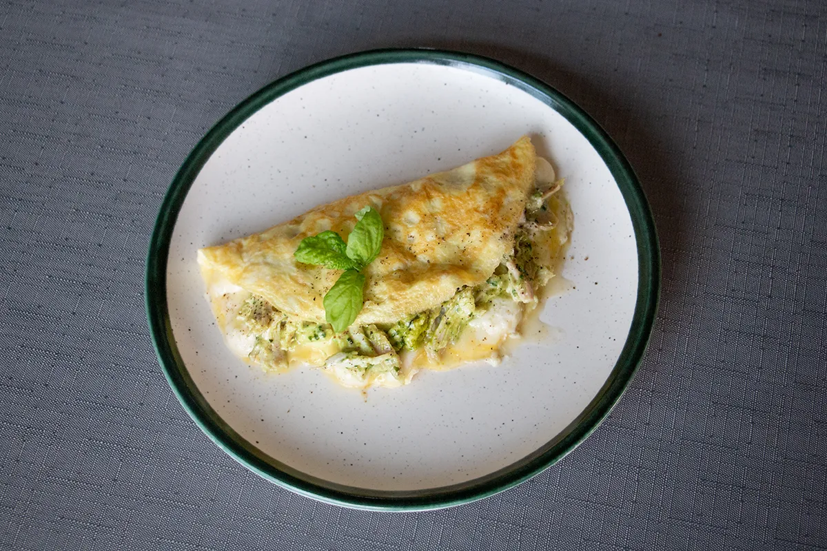 White and green plate with an omelette filled with pesto and chicken. Some basil leaves sit on top.