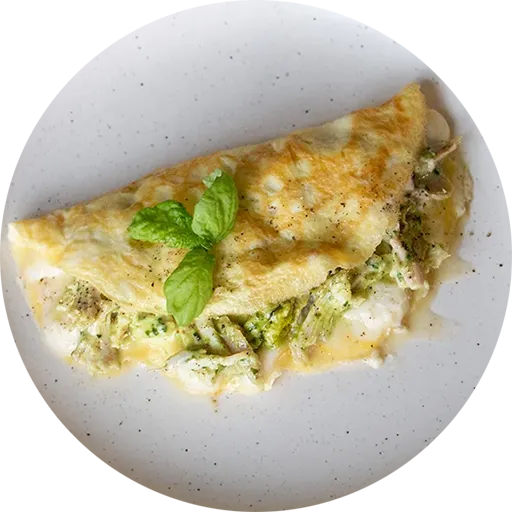 White and green plate with an omelette filled with pesto and chicken. Some basil leaves sit on top.