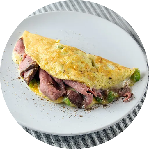 Omelette filled with roast beef and green beans on a white plate.