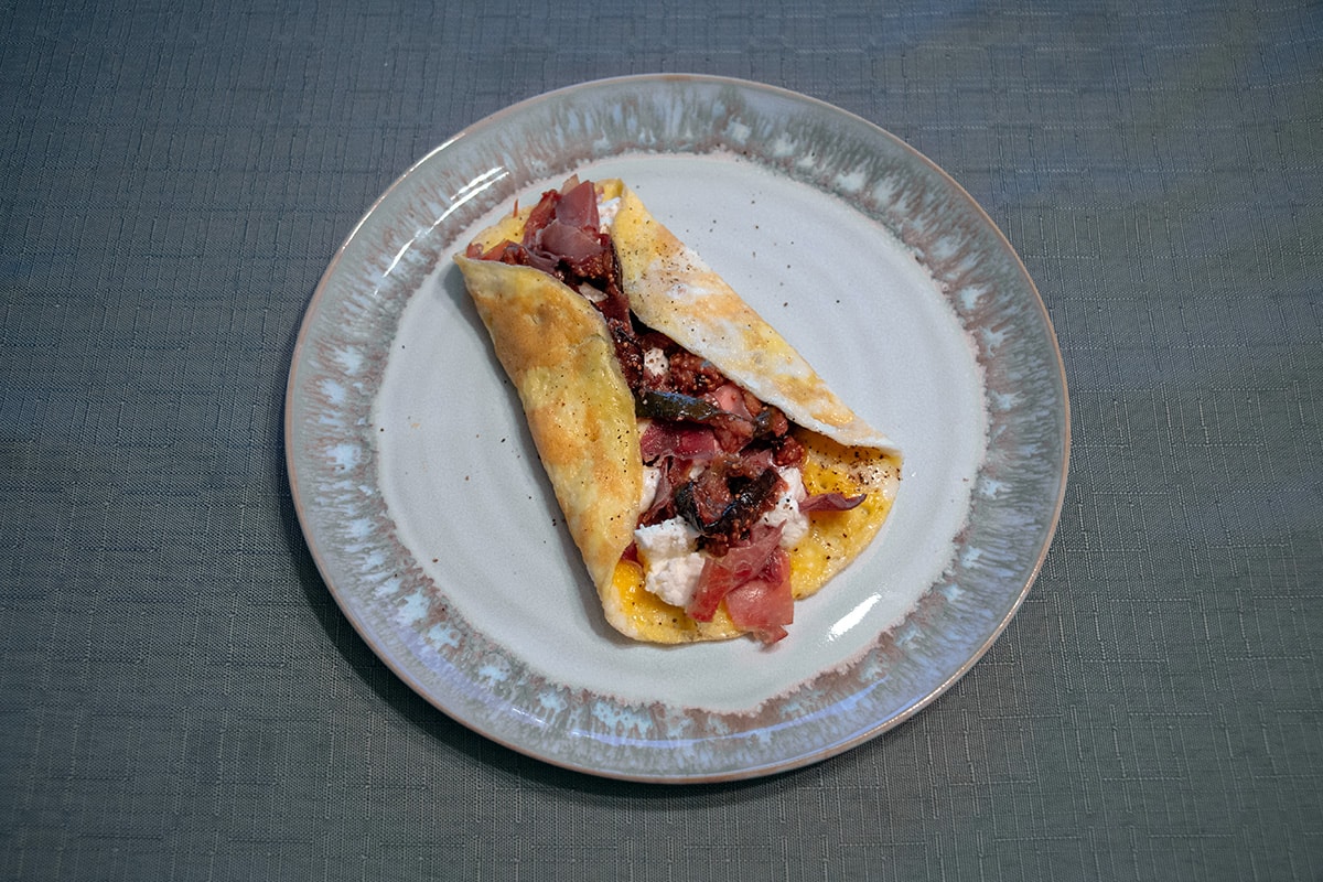 White and grey plate with an omelette filled with prosciutto, fig and goat cheese.