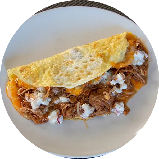 White plate with an omelette stuffed with cheese, pulled pork and a white sauce.
