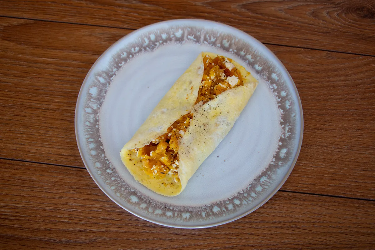White and grey plate with a rolled omelette filled with pumpkin and feta cheese.