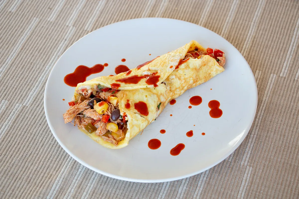 White plate with a rolled omelette filled with chicken, peppers, beans, corn and salsa.