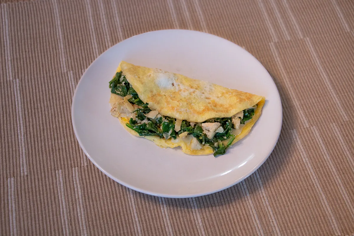White plate with an omelette filled with spinach, artichokes and cheese.
