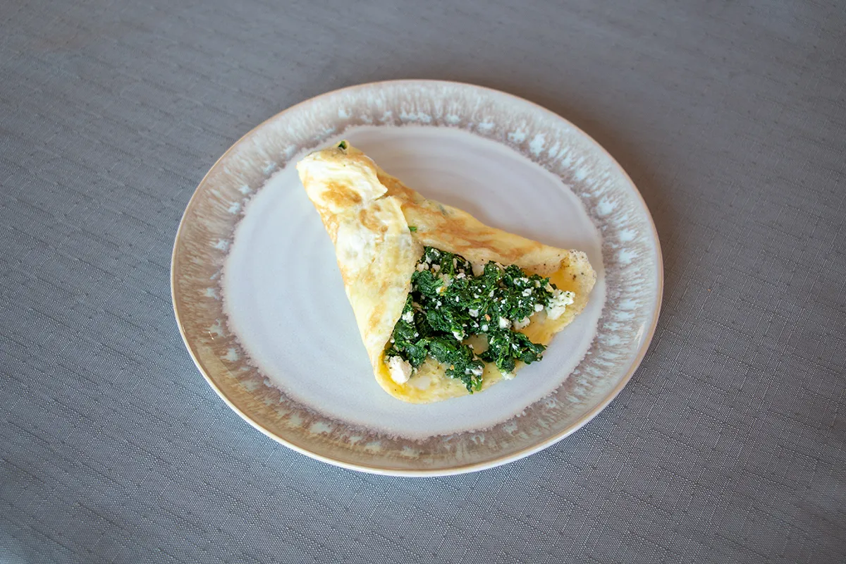 White and brown plate with an omelette stuffed with spinach and feta cheese.