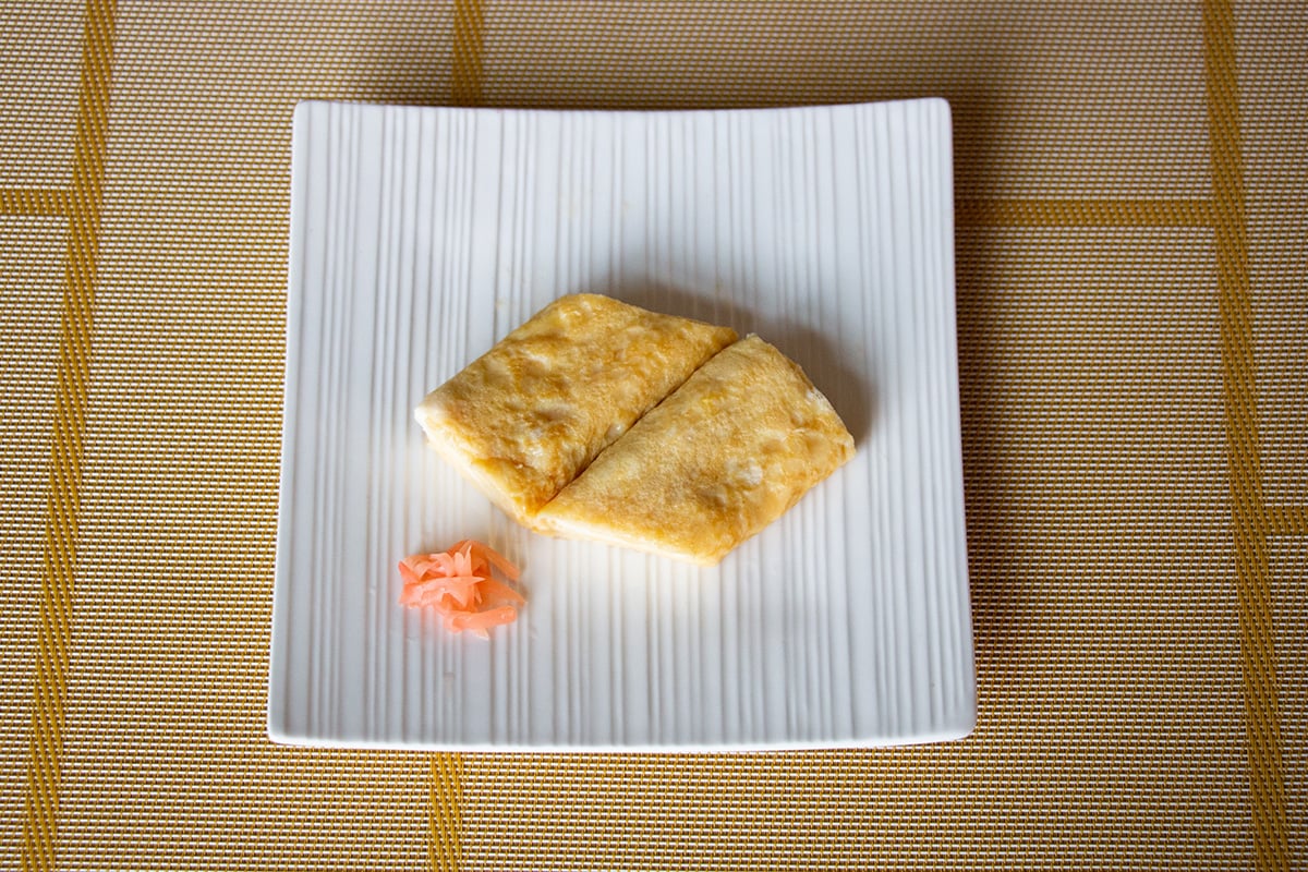 Square white plate with a rolled omelette and a small pile of pickled ginger.