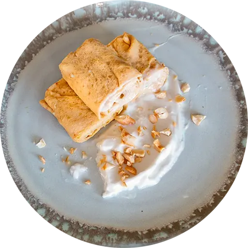 White and grey plate with a rolled omelette, coconut milk, and crushed cashews.