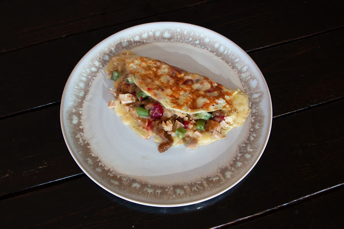 White and brown plate with an omelette filled with turkey, beans, stuffing and cranberries.