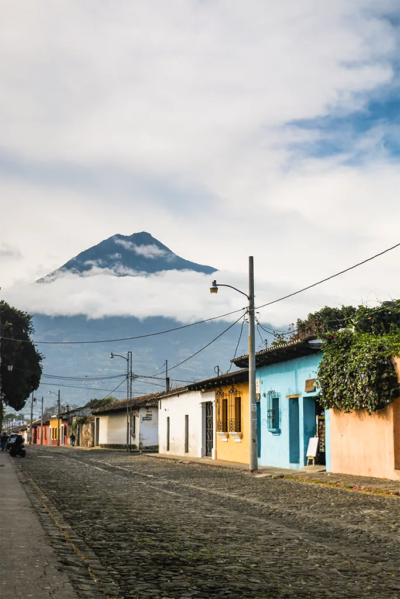 Yellow and blue buildings along a cobbled street with a towering volcano in the background.