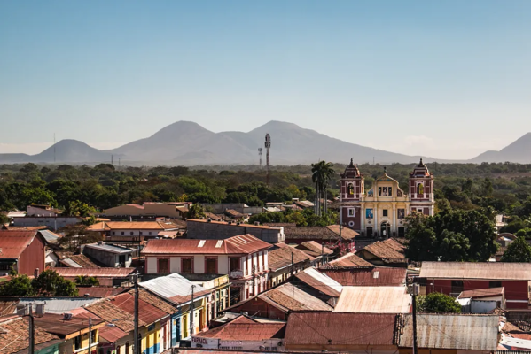 Overhead view of a colonial city in Latin America with a yellow and brown cathedral. Jungle and volcanoes are seen in the background.
