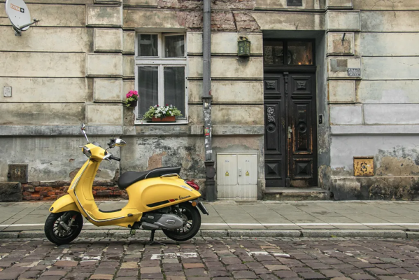 Yellow vespa on a stone street in front of a grey concrete building.